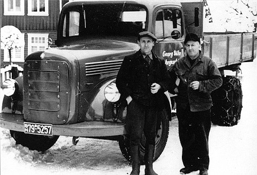 Zwei Männer in Arbeitskleidung stehen neben einem Pritschenlastwagen mit Schneeketten auf den Hinterrädern; auf der Fahrertür der Schriftzug Georg Bähr.